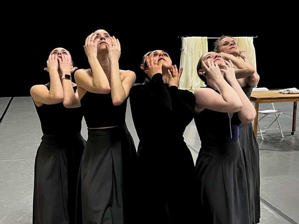 Members of Deos Contemporary Ballet cluster together in rehearsal for "Locked Doors." Their hands touch their cheeks as they look up in grief.