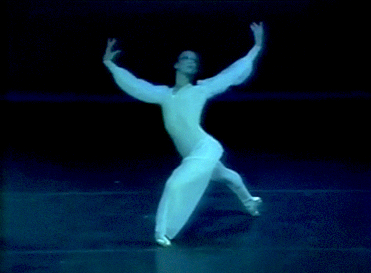 Sandra Fortune Green performs a ballet onstage, wearing a billowy white gown with long sleeves, white tights and pointe shoes. She poses in a deep lunge, pointing her right foot behind her, and lifts her arms up in a gentle curve as she looks up towards her left hand.