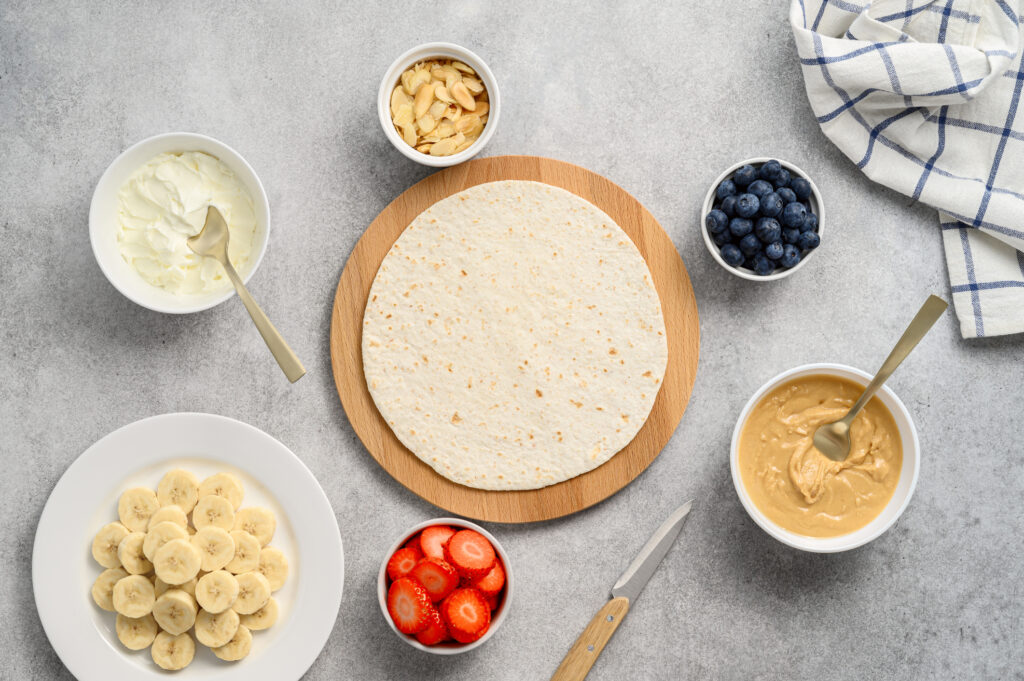 Tortilla cooking process with different fillings of peanut butter, banana, strawberry, blueberry, almond. Food trend. Sweet sandwich for breakfast. Trendy way of wrapping. Top view, copy space
