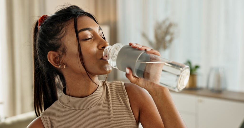 A young woman drinks water out of a reusable water bottle.