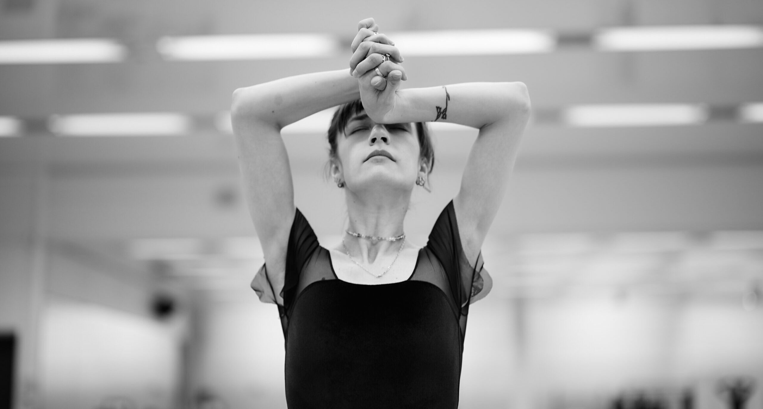 A close-up black and white shot of Max Richter in rehearsal. Richter clasps their hands and folds their arms in to rest her wrists on their forehead, eyes closed.