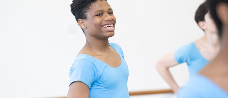 Anthony Madu, shown waist-up, smiles in ballet class wearing a bright blue shirt.