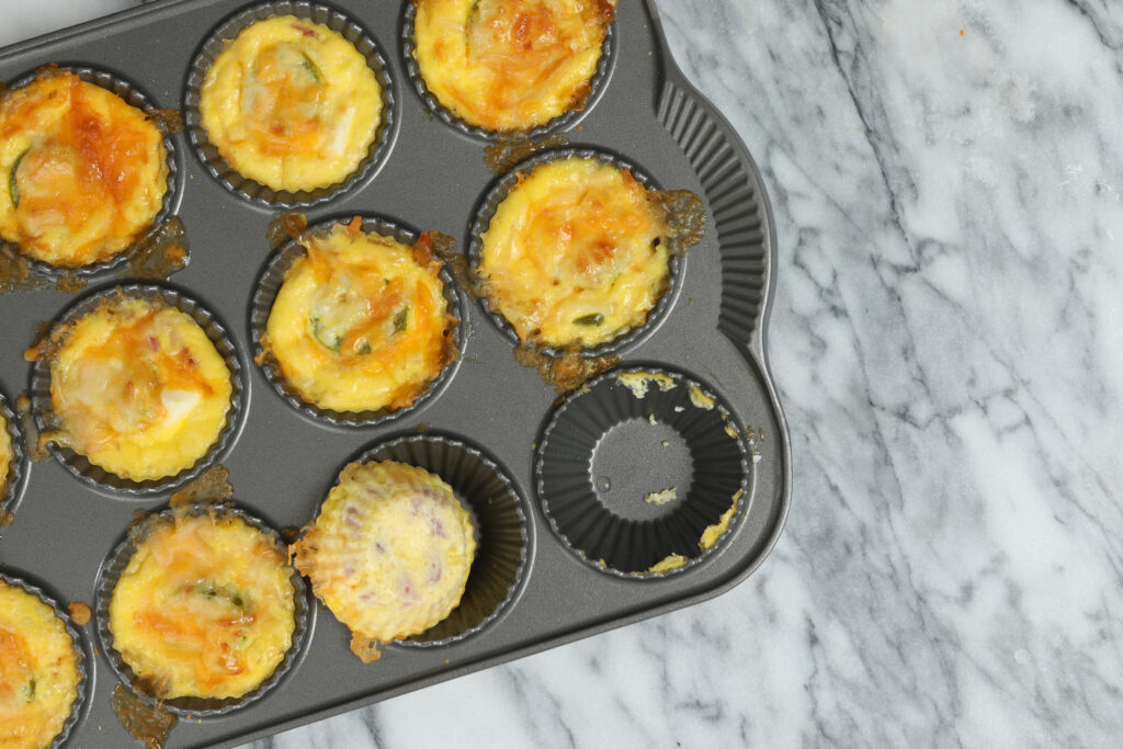 An overhead close-up photograph of a baking pan with freshly made egg bites, it appears the chef has already sampled one of them.
