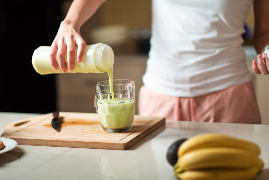 Woman pouring avocado and banana smoothie for a juice with healthy breakfast at home