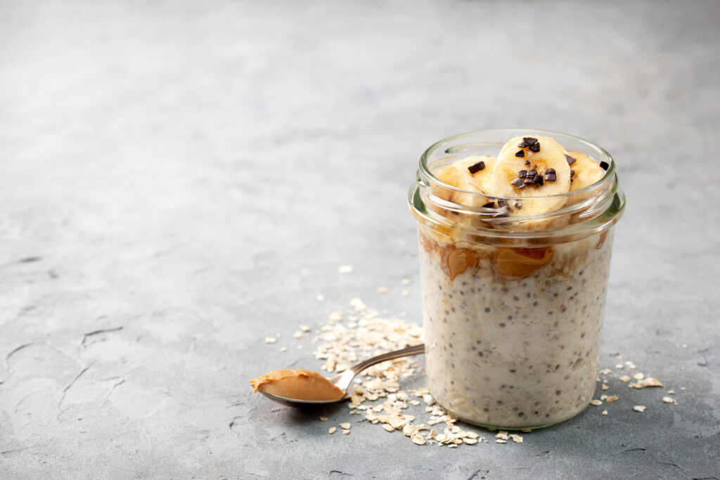 A mason jar of overnight oats and chia seeds, topped with banana slices and nut butter.