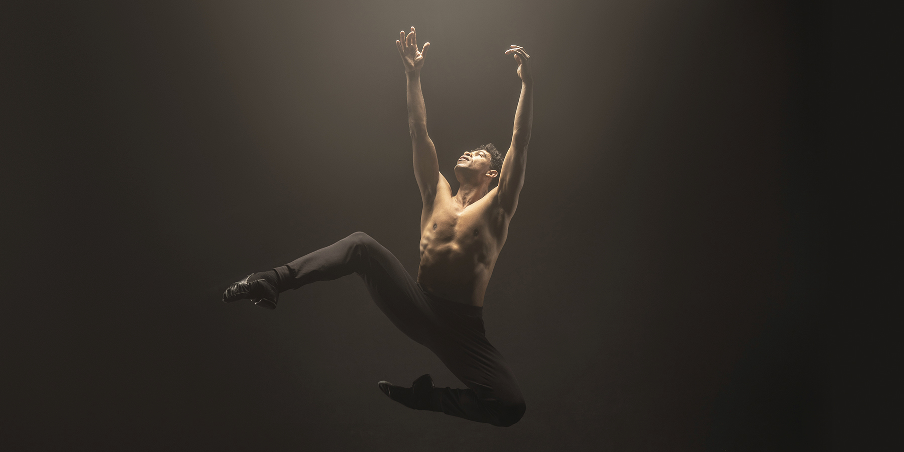 Carlos Acosta is suspended mid-air in a jump, reaching toward the sky with his legs bent