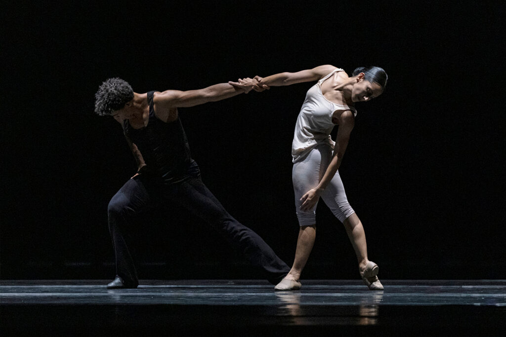 Carlos Acosta and Laura Rodriguez hold hands and lean away from each other in tendu derriere.