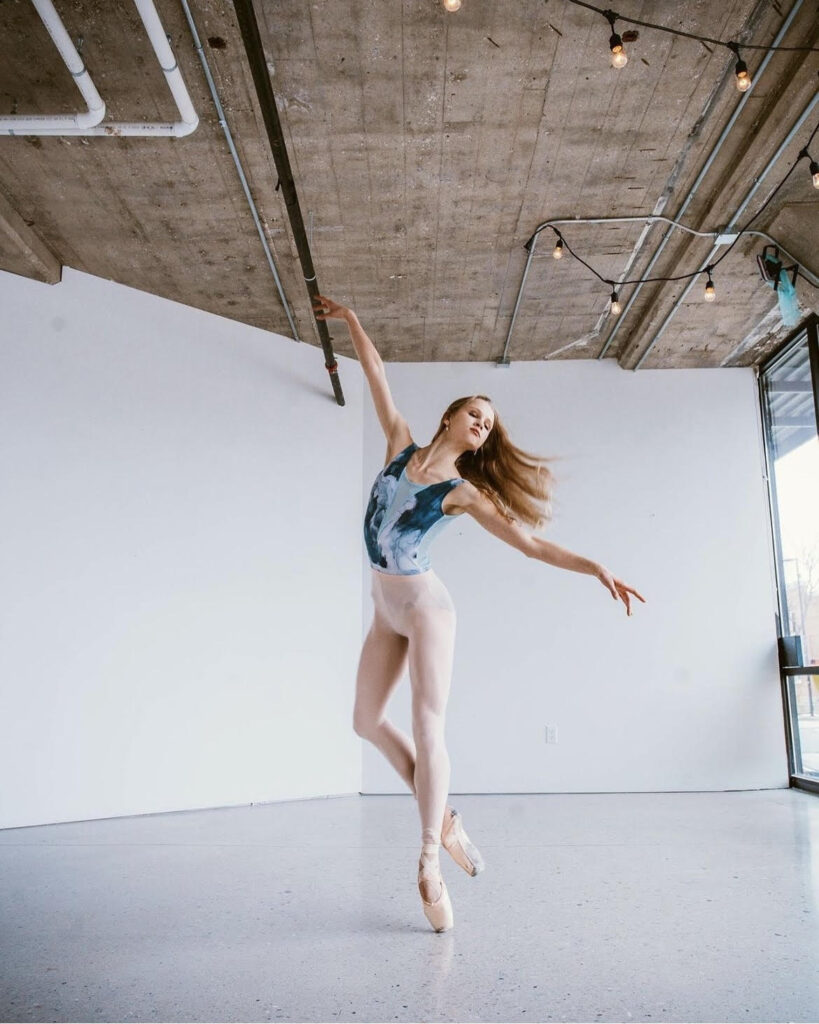 Taylor Ayotte poses on pointe in a cou de pied derriere on pointe.