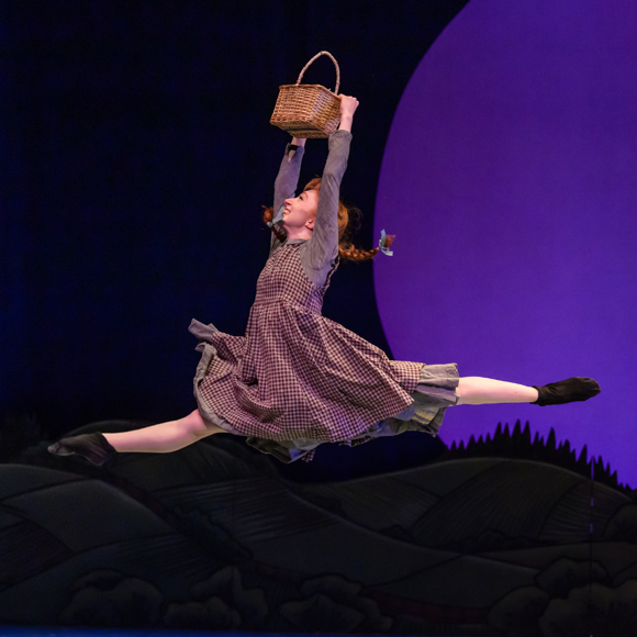 Hannah Mae Cruddas does a saut de chat in "Anne of Green Gables — The Ballet." She wears a gingham dress and holds a basket overhead.
