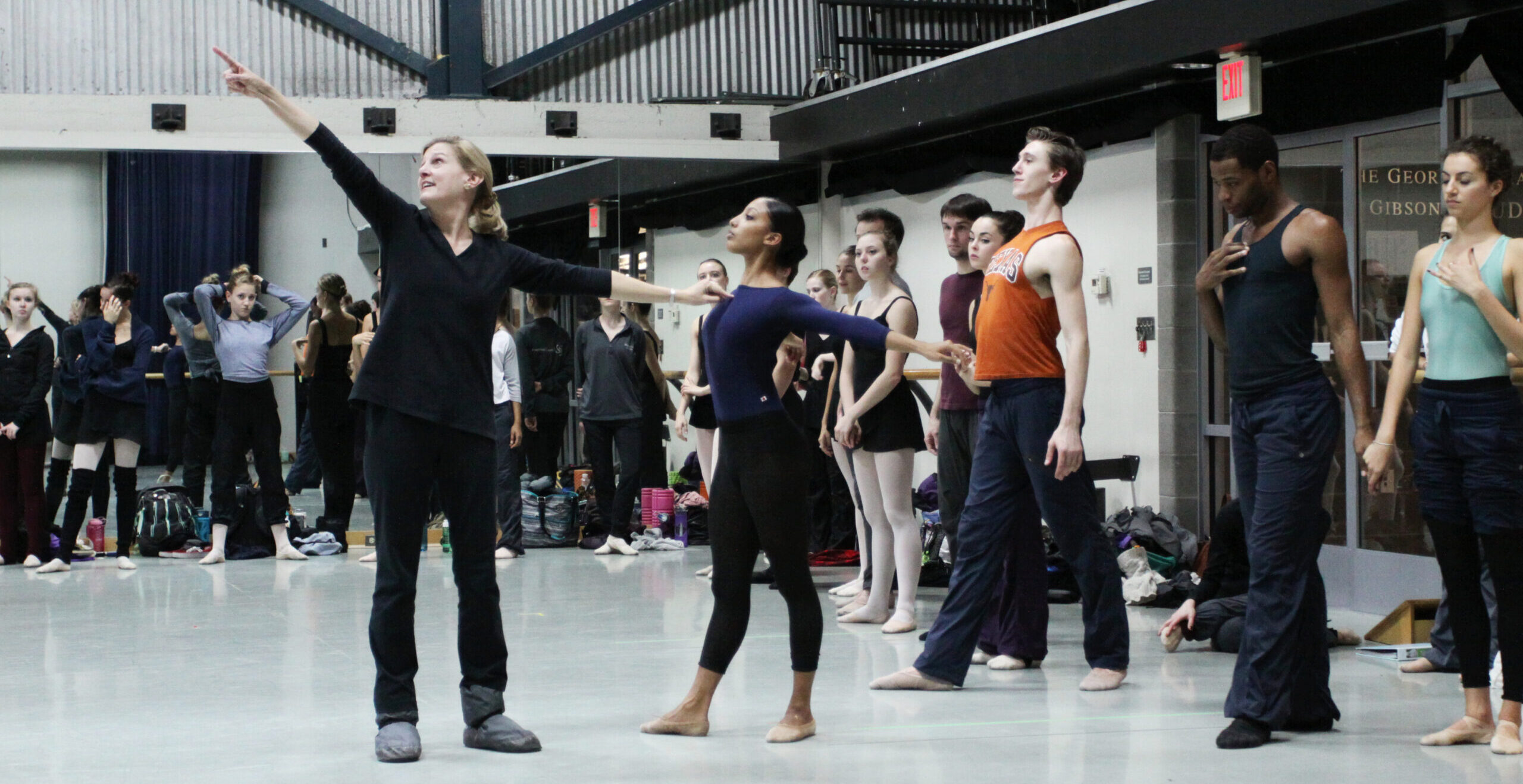 Stoner Winslett demonstrates an open allongé port de bras position in rehearsal with a large group of dancers.