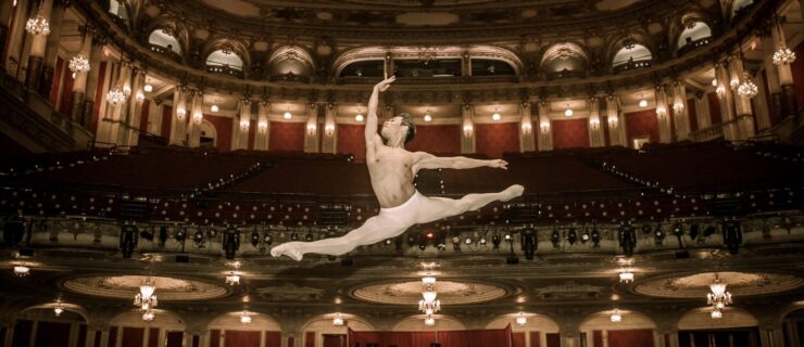 With a large, opulent theater house in the background, John Lam flies in a sauté split wearing white tights.