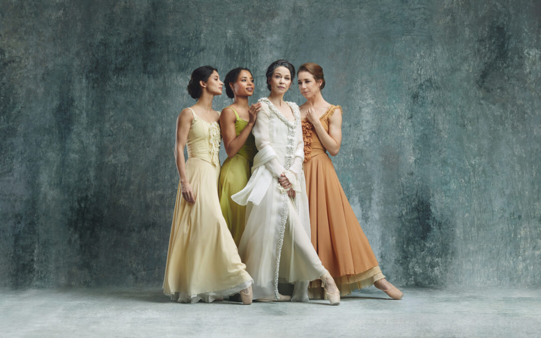 Four female dancers stand side-by-side in long, flowing dresses in yellow, green, white, and orange, L-R.