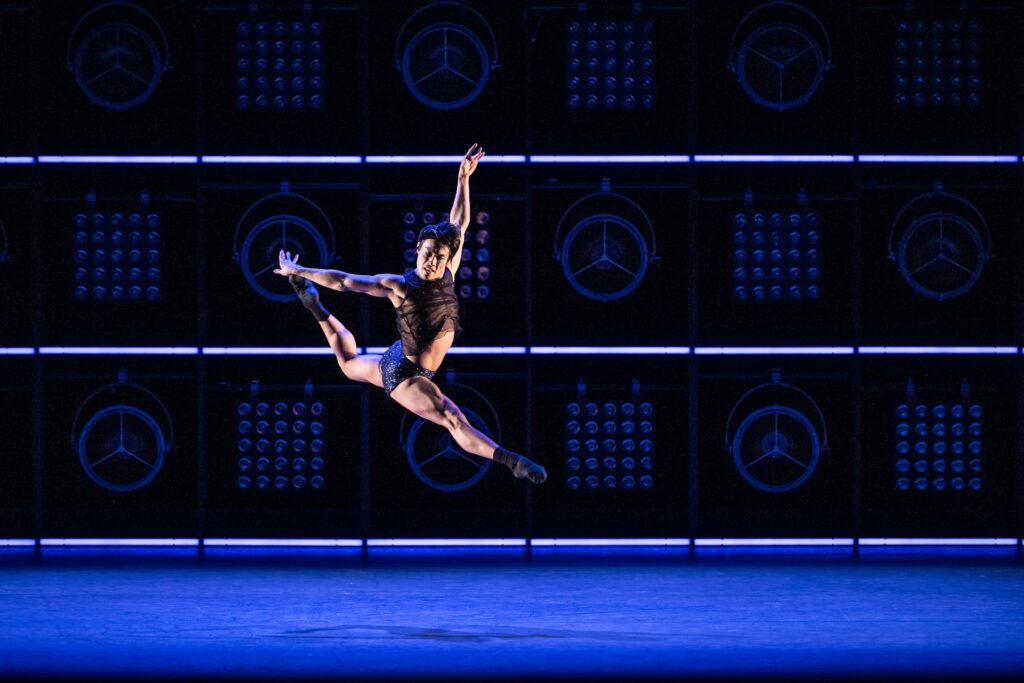 John Lam flies in a back attitude saut de chat, arms high in a stylized arabesque line. 