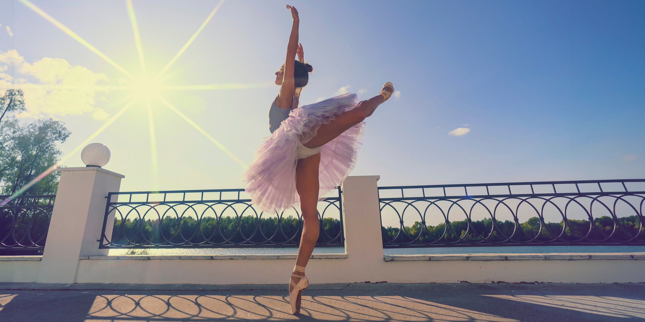 A young female ballet dancer in a tutu bodysuit and pointe shoes with beautiful feet makes an arabesque on a summer day on the terrace