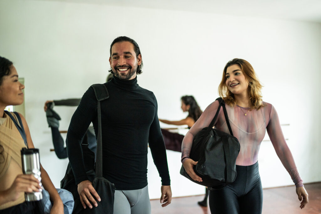 Three friends talk and laugh together as they walk in a dance studio.