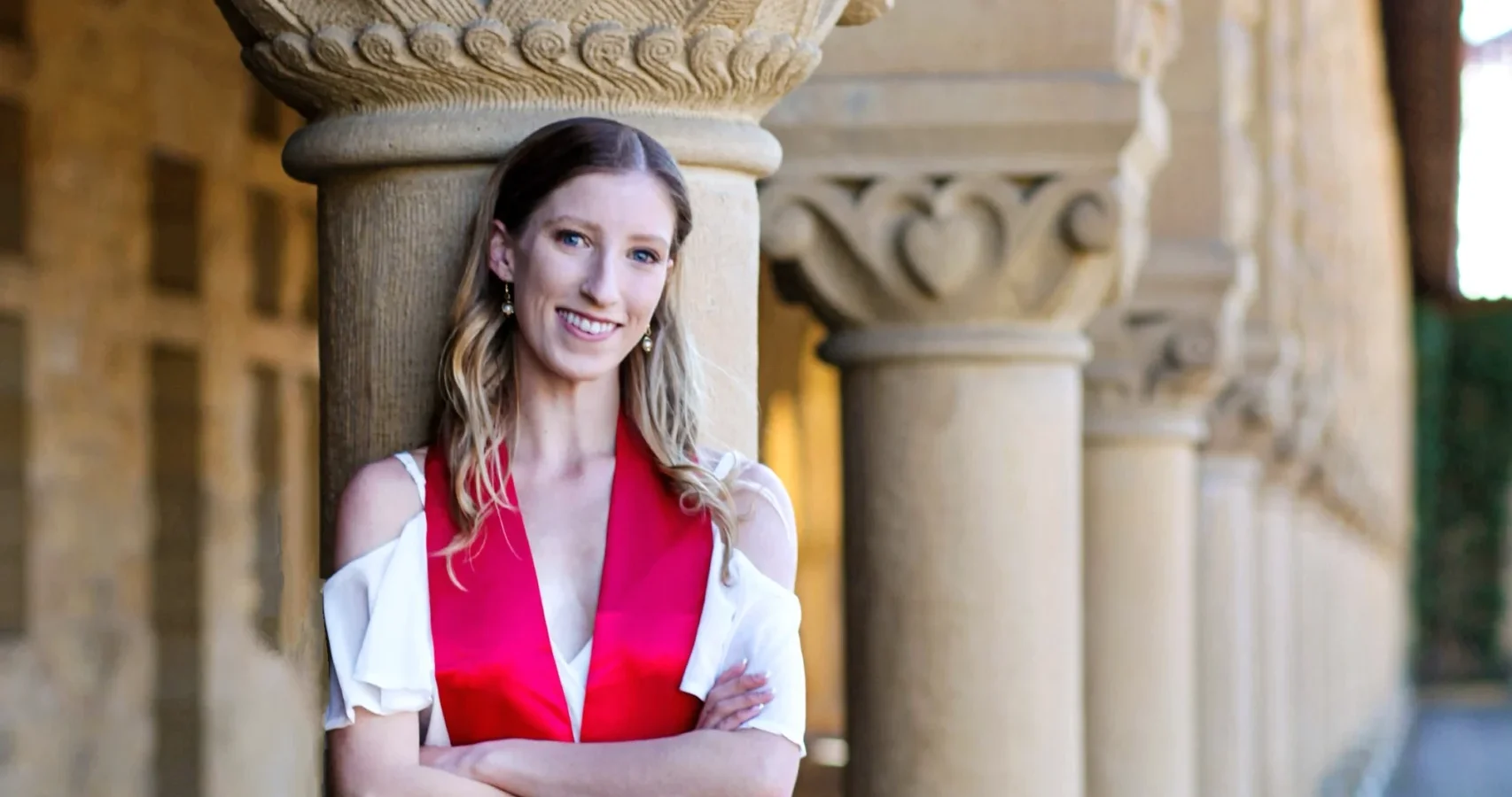 Ellie Prince poses at Stanford University, wearing a white dress and red stole.