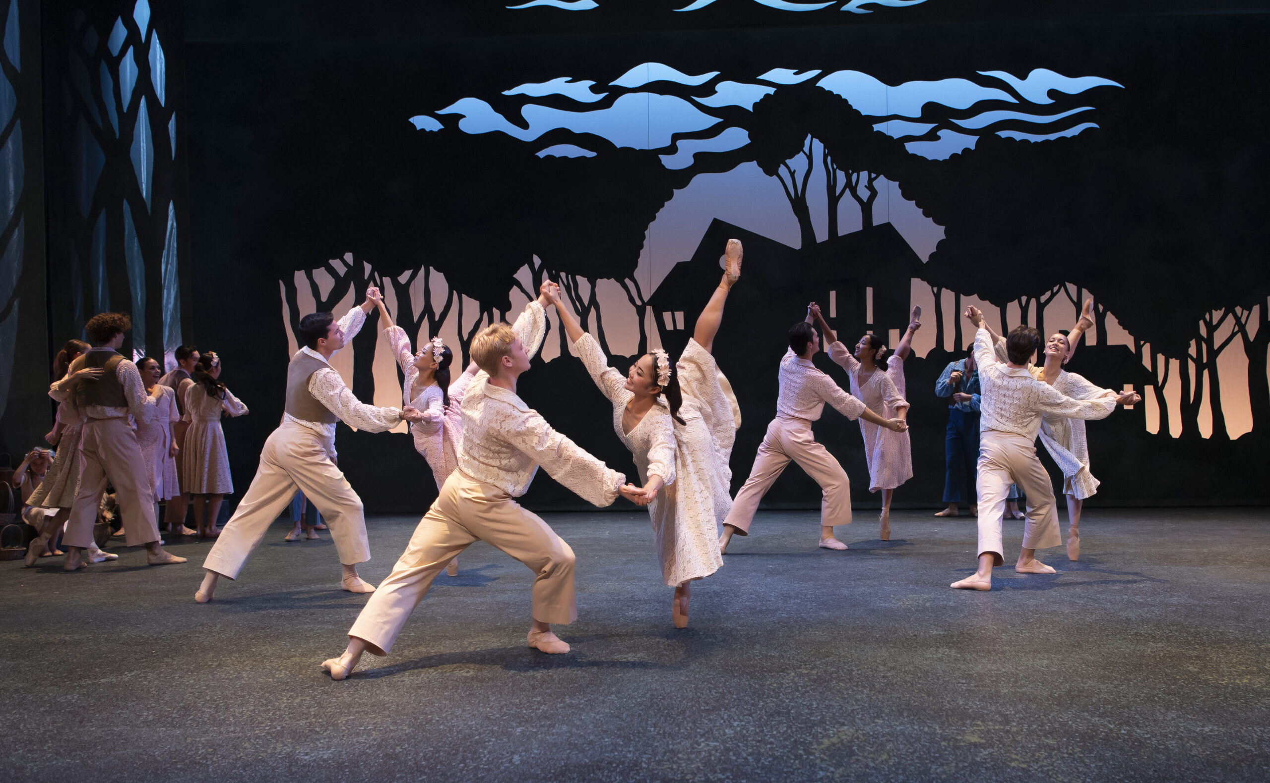 In front of a textured backdrop showing a countryside sunset, a group of four dancer pairs pose in a diamond shape. The women stand in penché on pointe, holding their partners' hands as they lunge in tendu derriere facing them. They all wear white, cream, and tan colors in peasant costumes that nod to Nordic folklore.