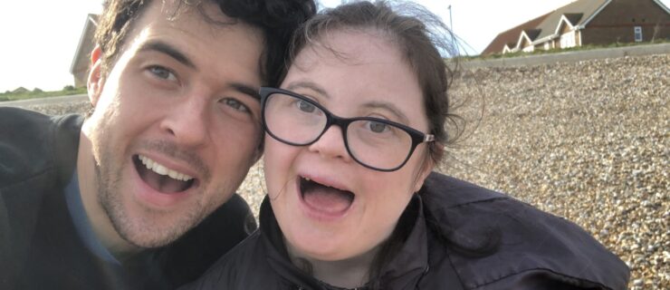 Thomas Forster stands very close to Louise Forster, theier heads touching as they take a selfie with big, open-mouthed smiles. They are outside and wearing jackets, with a road and houses in the background.