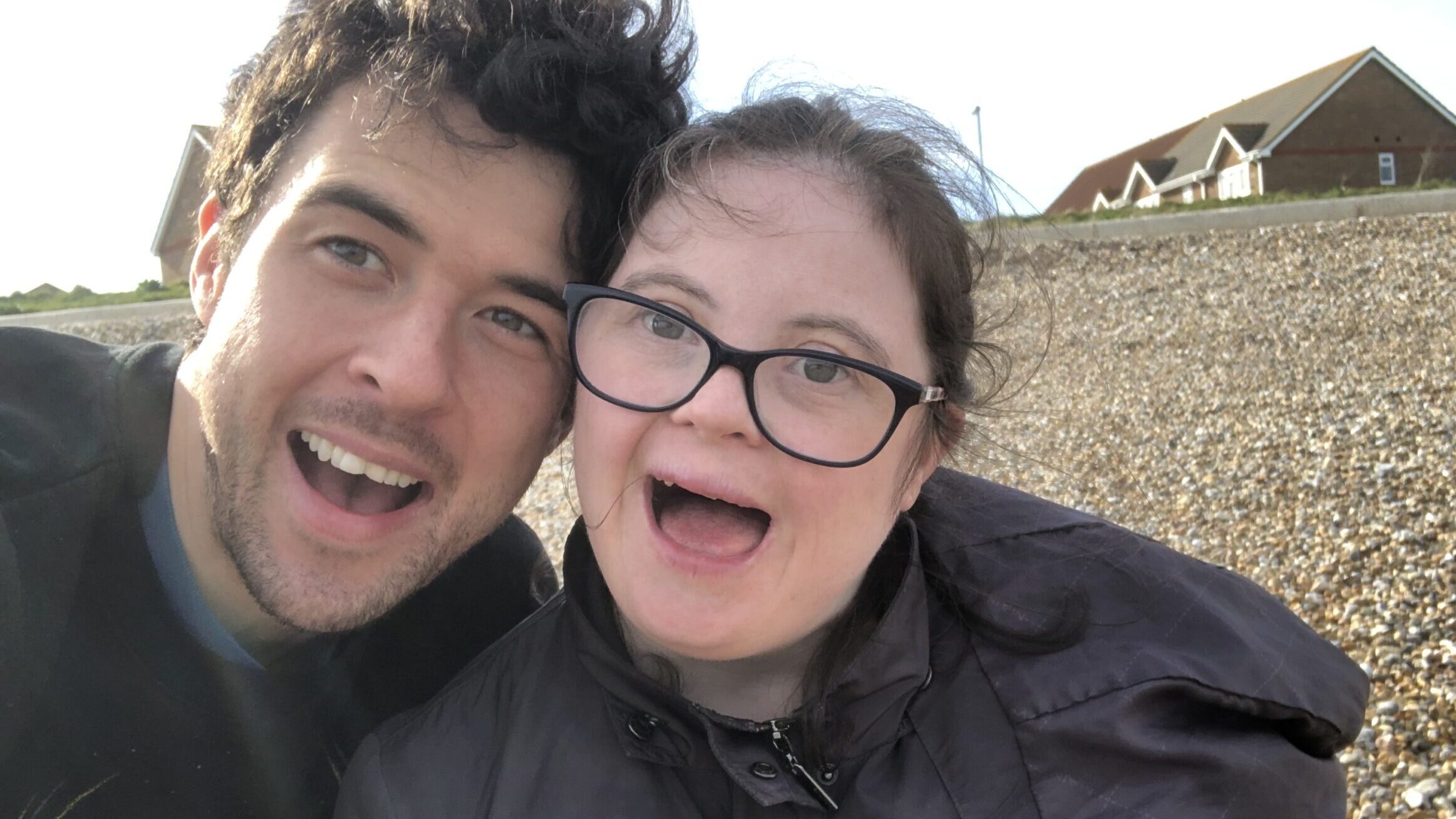 Thomas Forster stands very close to Louise Forster, theier heads touching as they take a selfie with big, open-mouthed smiles. They are outside and wearing jackets, with a road and houses in the background.