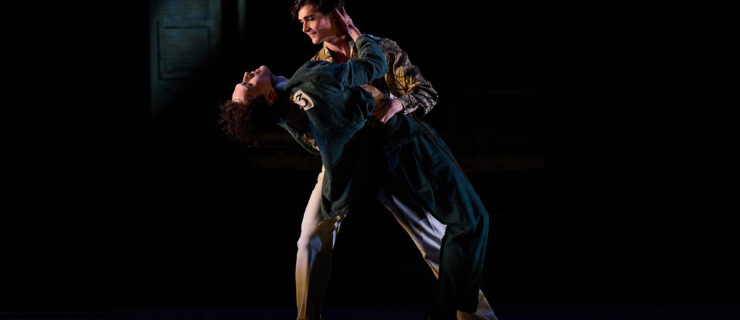 Benjamin Garrett and Callum Linnane dance onstage together, the former holding the latter as he leans backward.