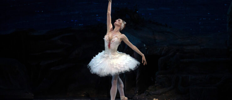 Gillian Murphy performs as Odette in a white pancake tutu with feathers and a red mark on her chest. She stands in a tendu derriere, one arm extended to the sky as if a wing as the other drapes gracefully at her side. She lifts her chin with a passionate, emotional look on her face.