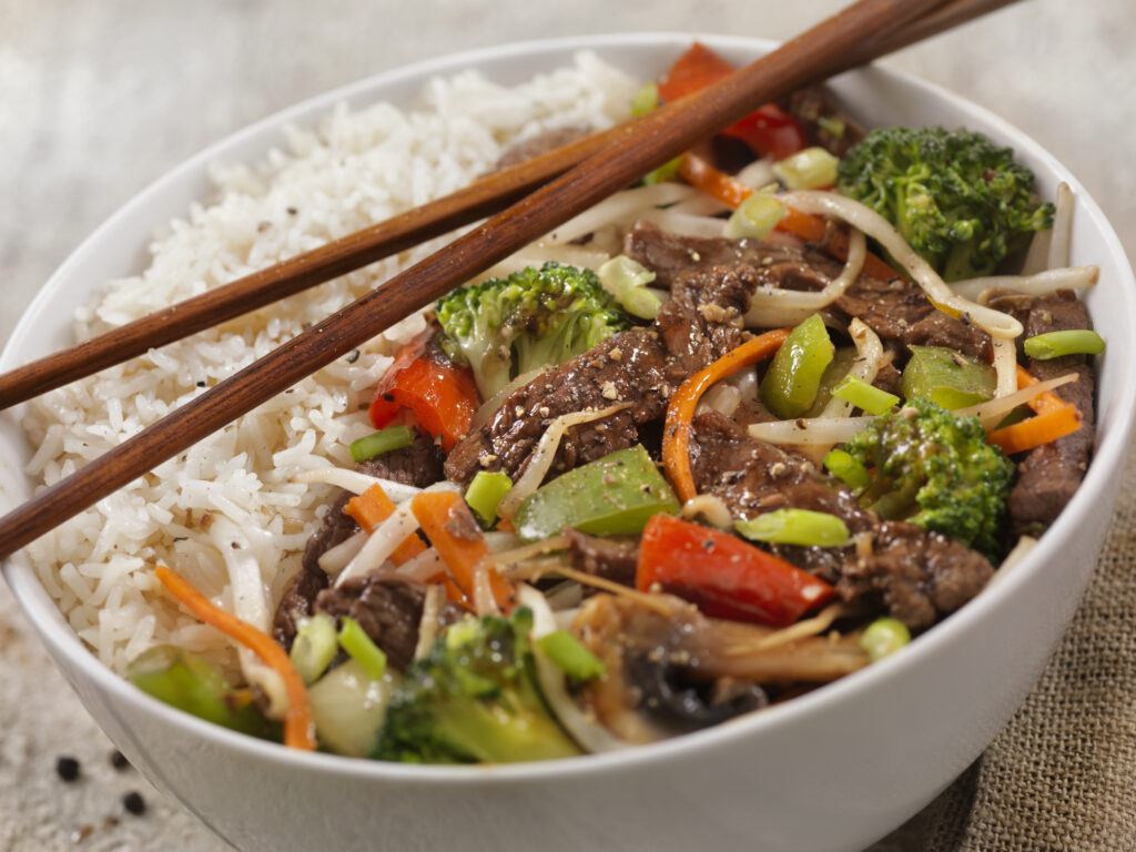 A peppered beef and vegetable rice bowl with sauce.
