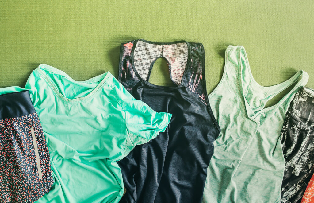 A collection of various athletic and dance wear is pictured. There are a couple leotards in shades of green and black, as well as some sports shorts and leggings in vibrant patterns.