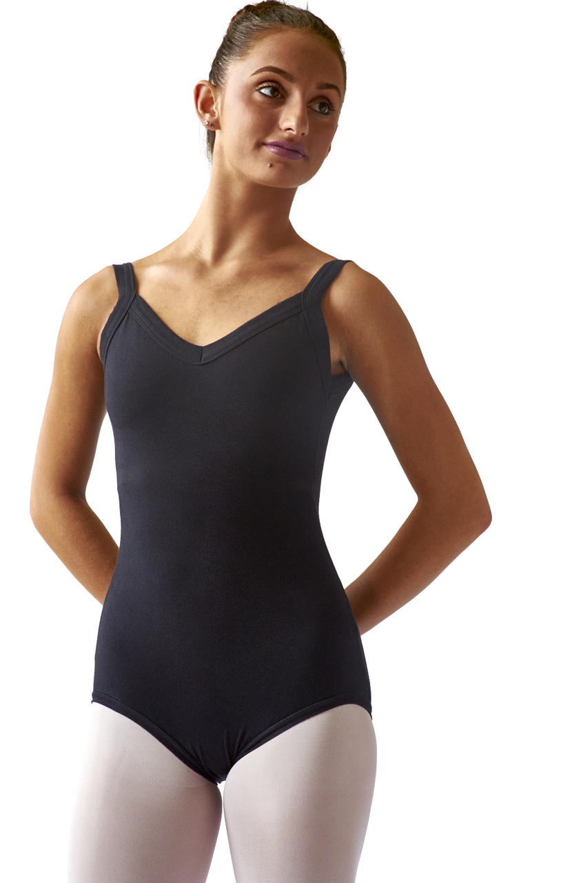 A young female dancer poses with her arms behind her back in front of a white backdrop. She wears a black leotard with tank straps and pink tights.