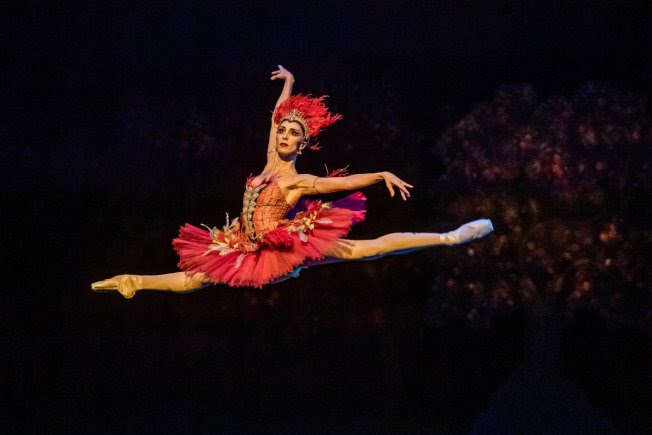 Itziar Mendizabal flies in a saut de chat onstage wearing a Firebird costume with a bright red feather headress.