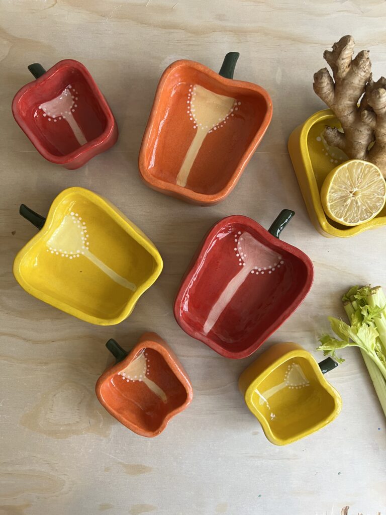 An overhead shot of dishes shaped like halves of bell peppers in yellow, orange, and red.