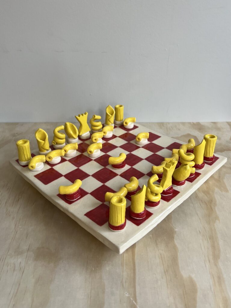A chess set with yellow pasta-shaped pieces on a red and white checkered base.