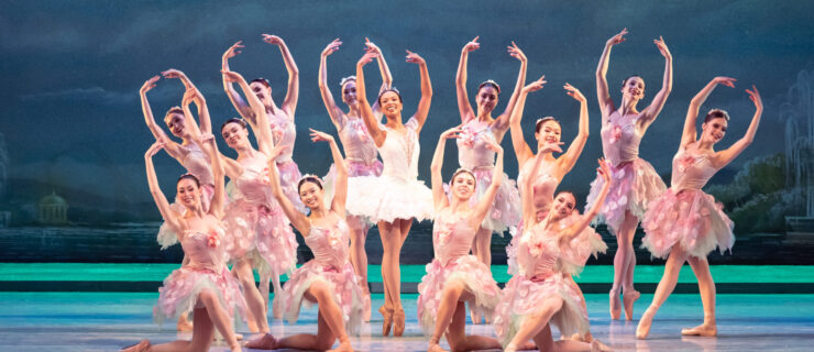 Onstage, Felecia Baker poses in sous-sus on pointe in a white, ruffly tutu with lace details, arms in high fifth. Around her, corps dancers dressed in cherry blossom dresses pose for a final tableau.