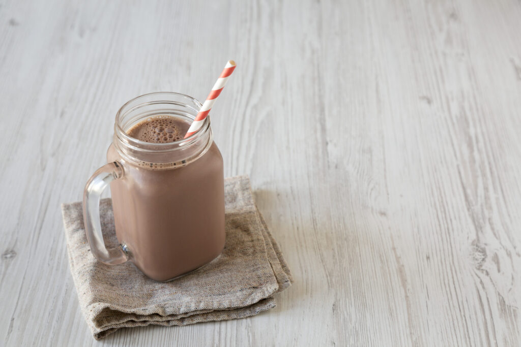 On a table, a mason jar filled with chocolate milk, with a red and white striped straw.