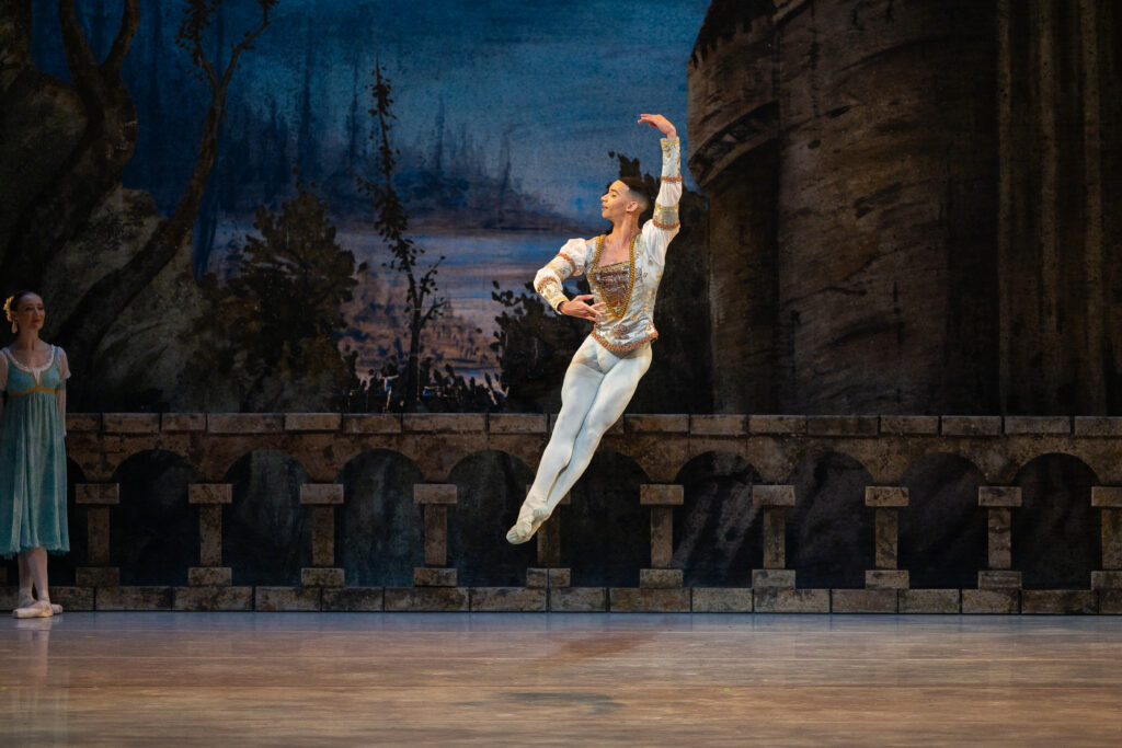 Randolph Fernandez performs an assemble on a dark stage with a painted lake in the background.