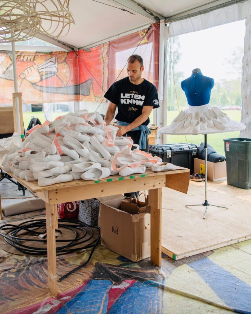 In a costume shop with big windows, Guzman stands behind a table piled high with white points shoes.