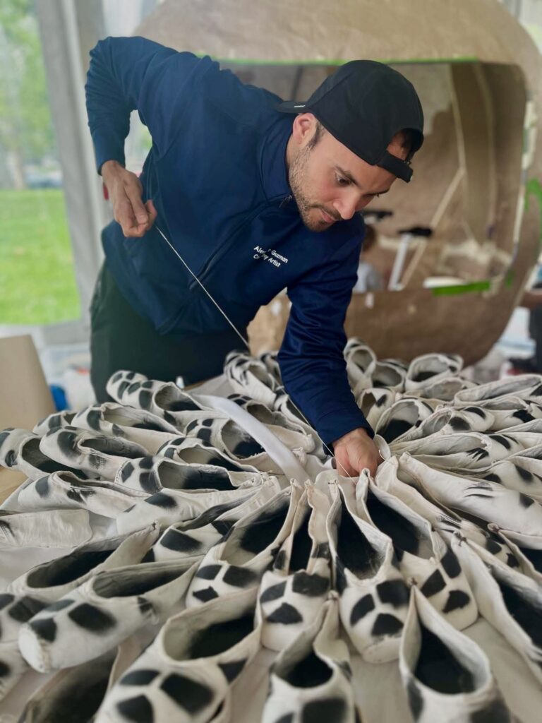Guzman leans over a cluster of white pointe shoes with black spots painted on them.