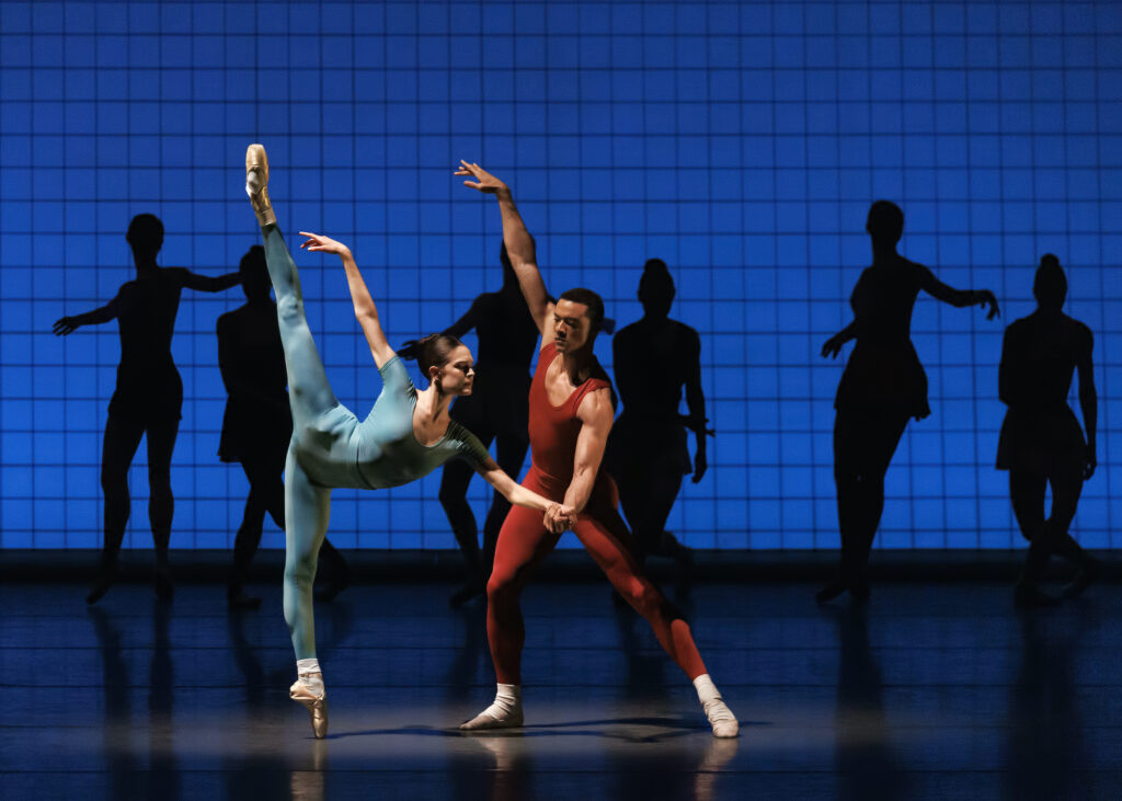 Ava Sautter, costumed in a blue unitard does a penché on pointe as her partner, Preston Chamblee, lunges slightly toward her and holds her left hand, raising hi right arm high to the side. They perform in front of a blue backdrop with gridlines and the silhouettes of six female dancers in mid-movement.
