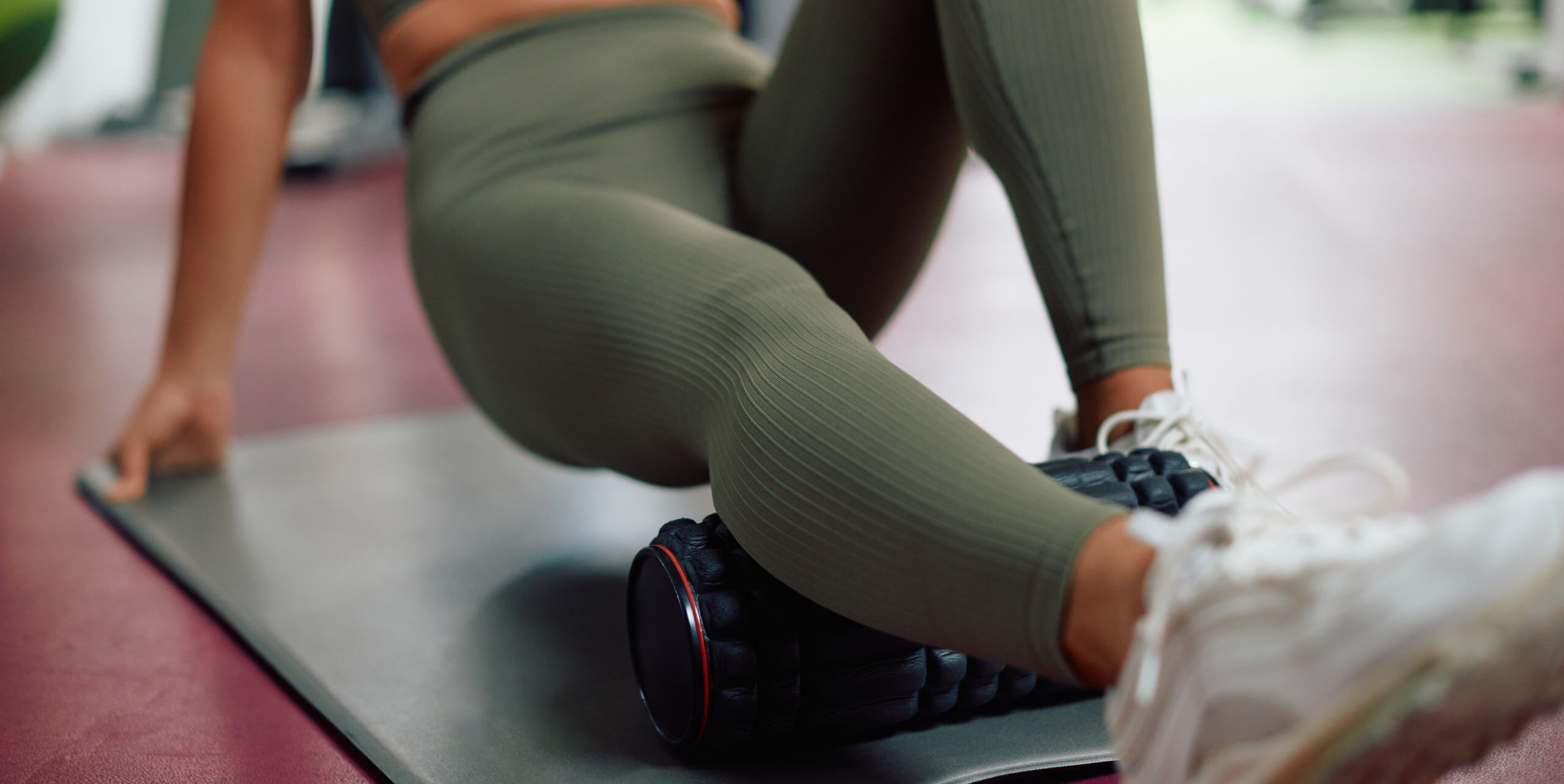 Close-up of athlete massaging her leg with foam roller in a gym.