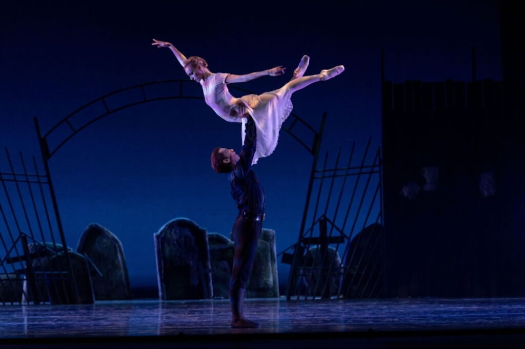 Parker Brasser-Vos lifts Jennifer Hackbarth above his head. Hackbarth crosses one leg over the other gently as she arches up, looking down at Brasser-Vos and extending her arms long in arabesque.