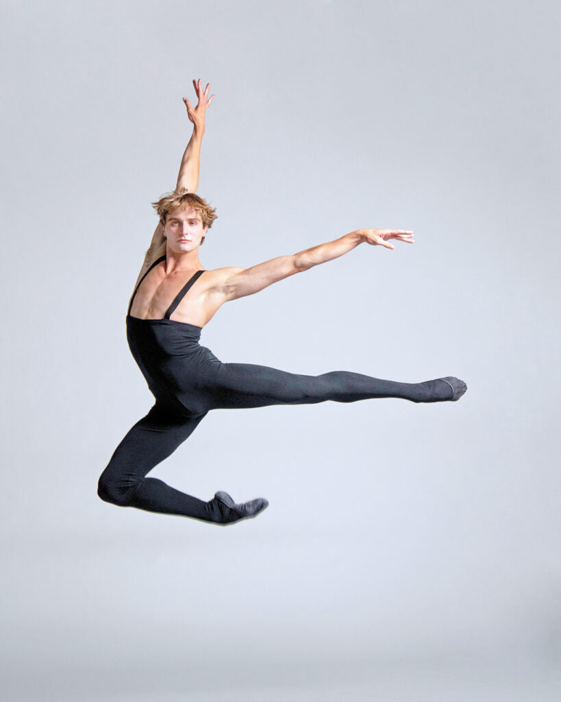 David O'Matz is captured mid-leap, front knee tucked up beneath him and back leg extended in arabesque.