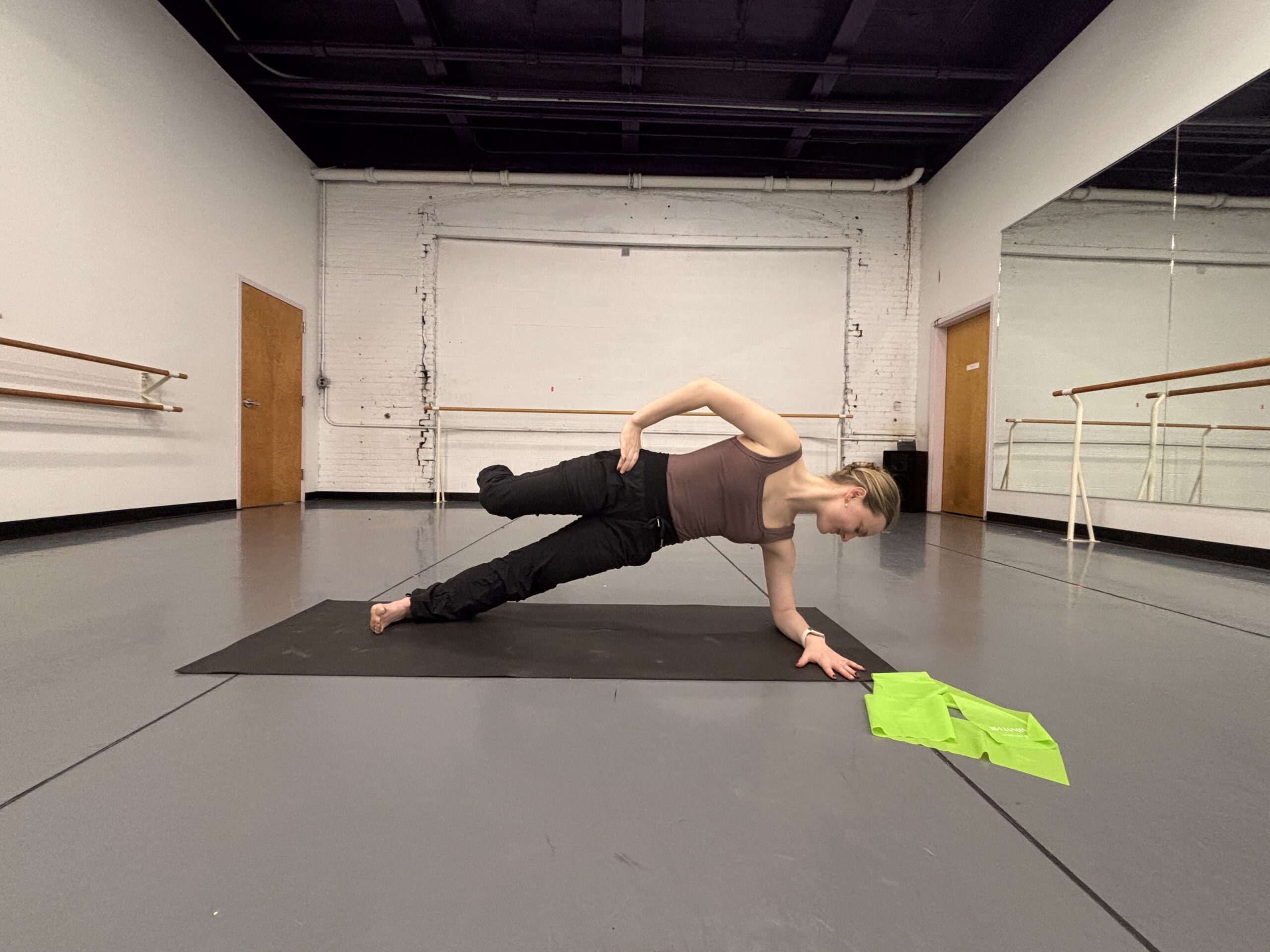 Lydia Marbach does a side plank with the top leg lifted and shifted backward in parallel, her knee at a 90 degree angle and her shin facing the side wall.