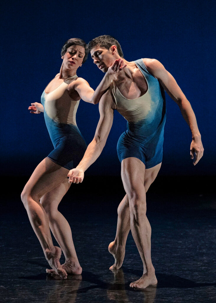 Anderson Da Silva performs alongside a fellow company member. Both are barefoot and wear blue and white biketards.