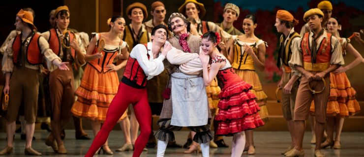 Val Caniparoli—costumed as Don Quixote in breeches, a neck scarf and a curled mustache—stands onstage at the center of a crowd, his arms crossed, smiling slightly. The dancers playing Basilio and Kitri hang adoringly on his arms.