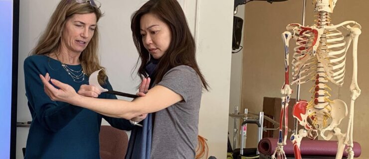 Dr. Linda Bluestein stretches out kinesiology tape to apply to a patient's elbow. The patient, arm lifted with a slight bend, looks down at the tape with concentration.