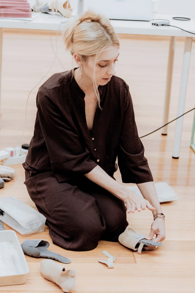 Sophia Lindner kneels on the floor while holding a 3-D printed shoe Act’ble founder.