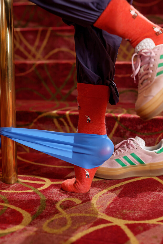 Close up of Sakamoto's foot in a red "Romeo and Juliet" sock, in releve with a blue TheraBand wrapped around her heel
