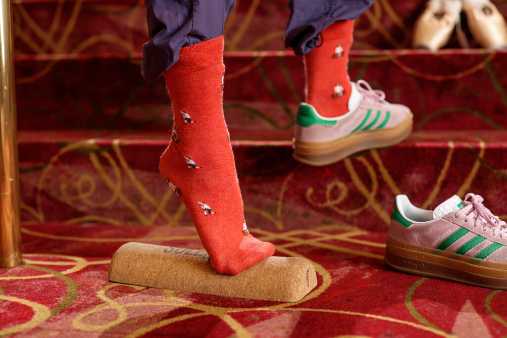 Close up of Sakamoto's foot in a red "Romeo and Juliet" printed sock, in releve on top of a half foam roller