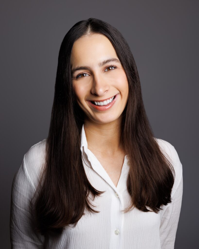 Danielle Farzanegan is shown from the waist up. She wears a. white button-down shirt. She has long dark hair parted down the middle and smiles towards the camera.