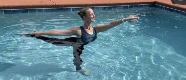 A woman poses in first arabesque outside in a pool.