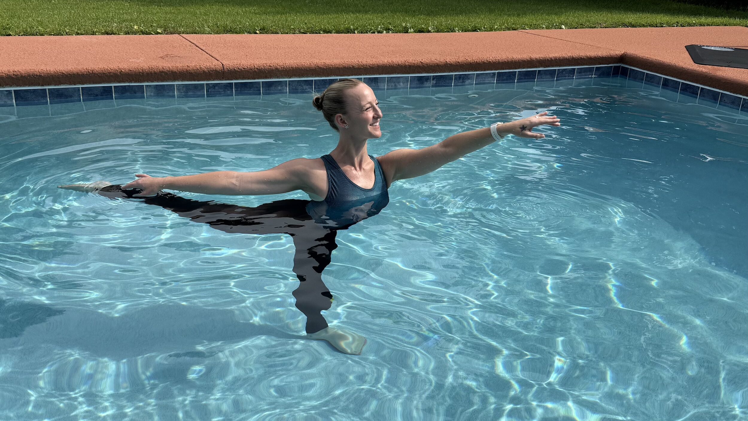 A woman poses in first arabesque outside in a pool.